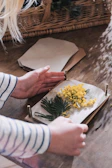 Close-up of hands delicately assembling a floral-themed junk journal with fabric and lace.