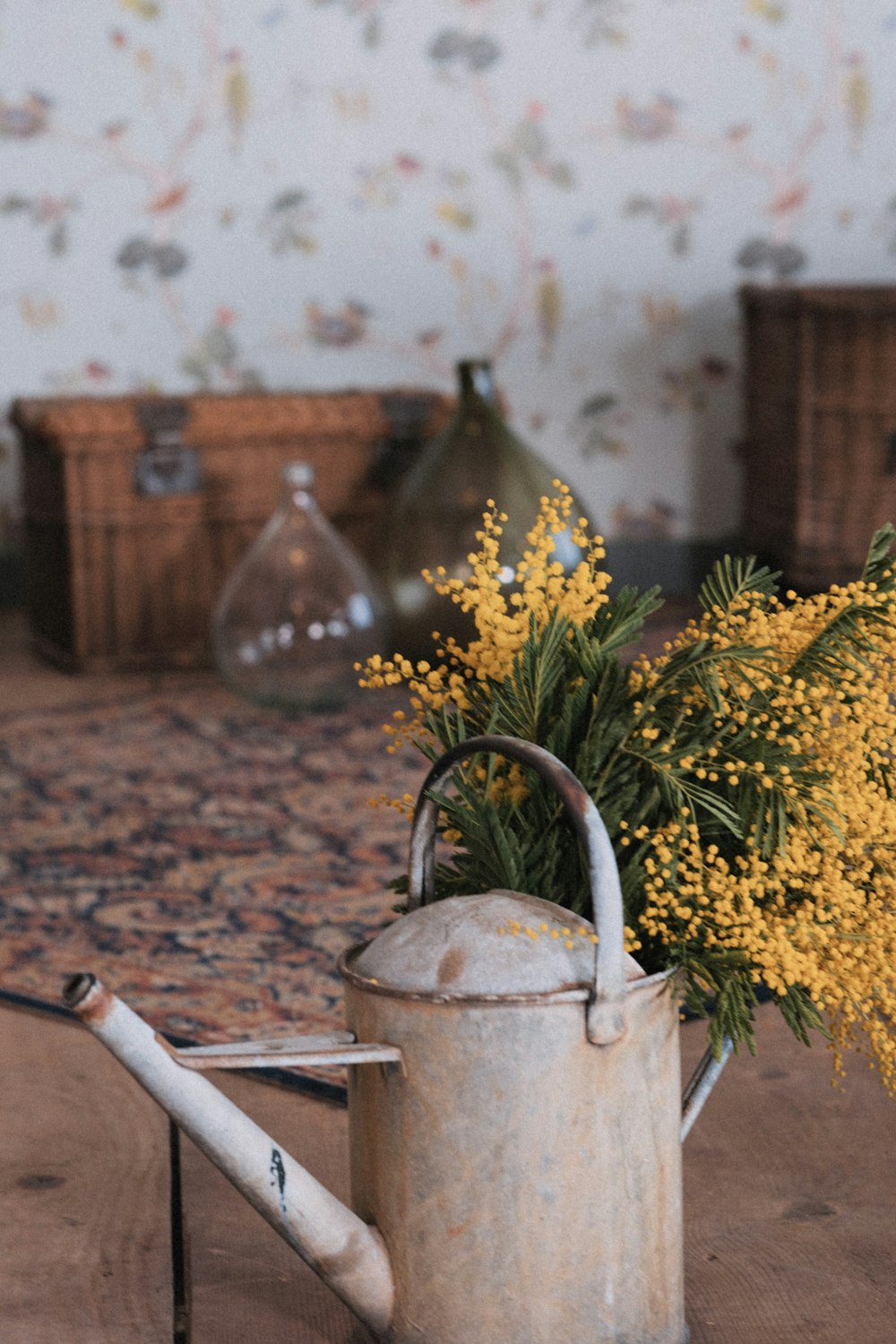 a watering can filled with yellow flowers on top of a wooden table