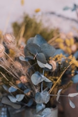 Close-up of a floral craft arrangement featuring dusty rose and sage green blooms in a rustic vase.