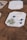 A wooden surface features rectangular coasters decorated with botanical elements. One coaster prominently displays a green fern, blue flowers, and white petals artistically arranged. Other coasters are partially visible with similar natural motifs.