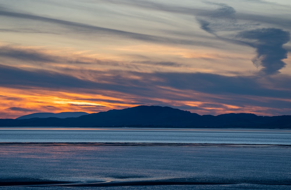 a sunset over a body of water with mountains in the background