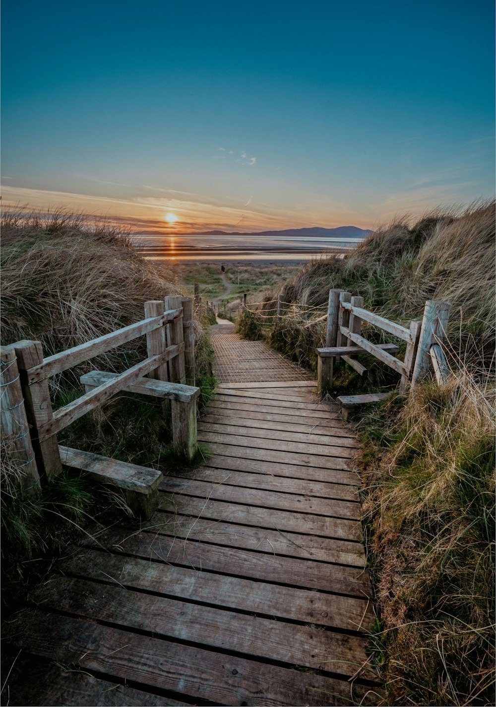 a wooden path leading to a beach at sunset