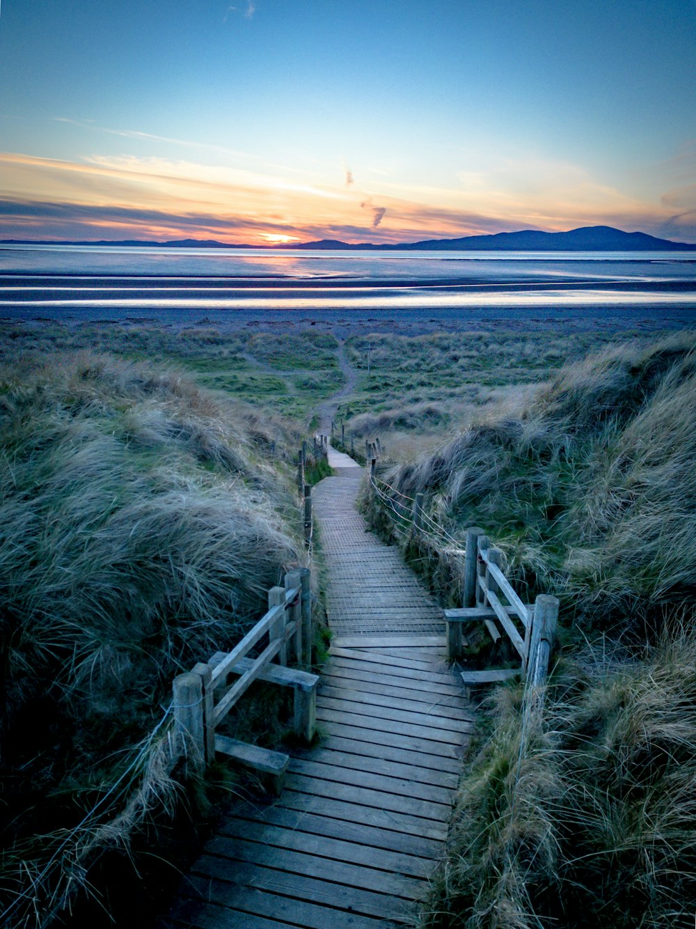 a wooden path leading to the beach at sunset