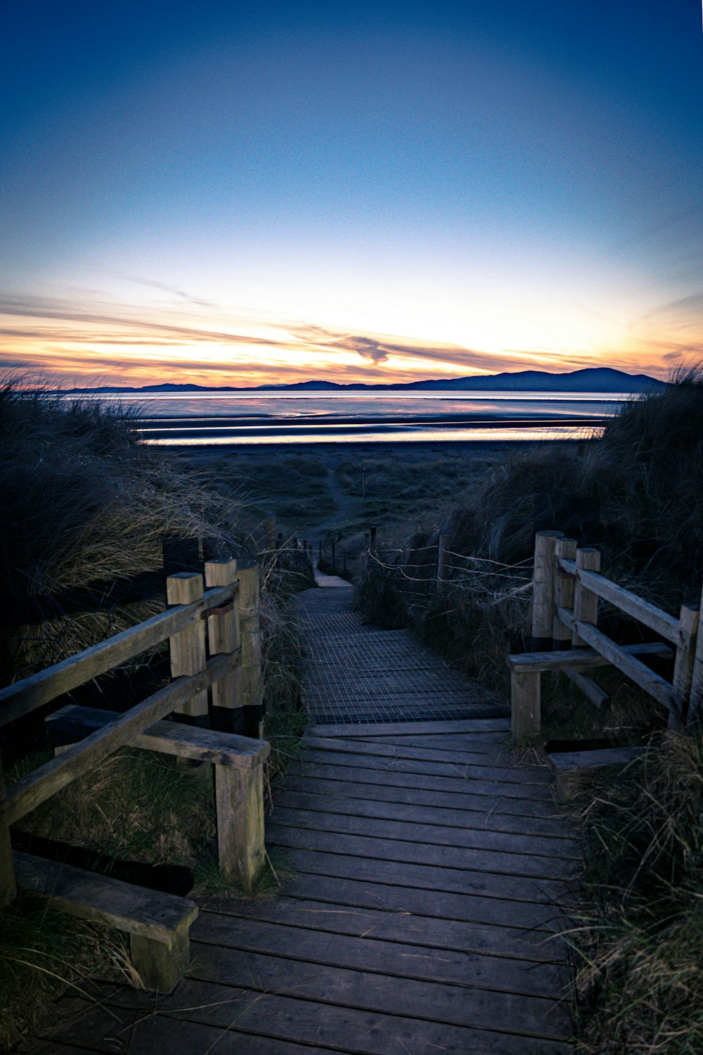 a wooden path leading to a beach at sunset