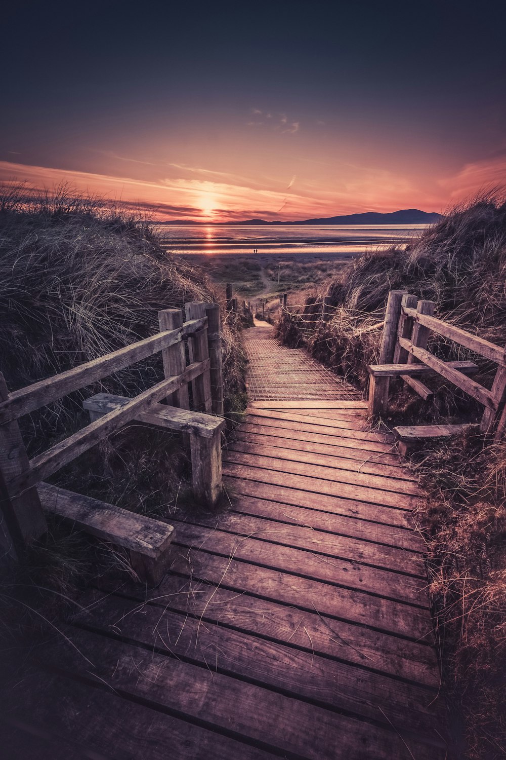 a wooden path leading to the beach at sunset