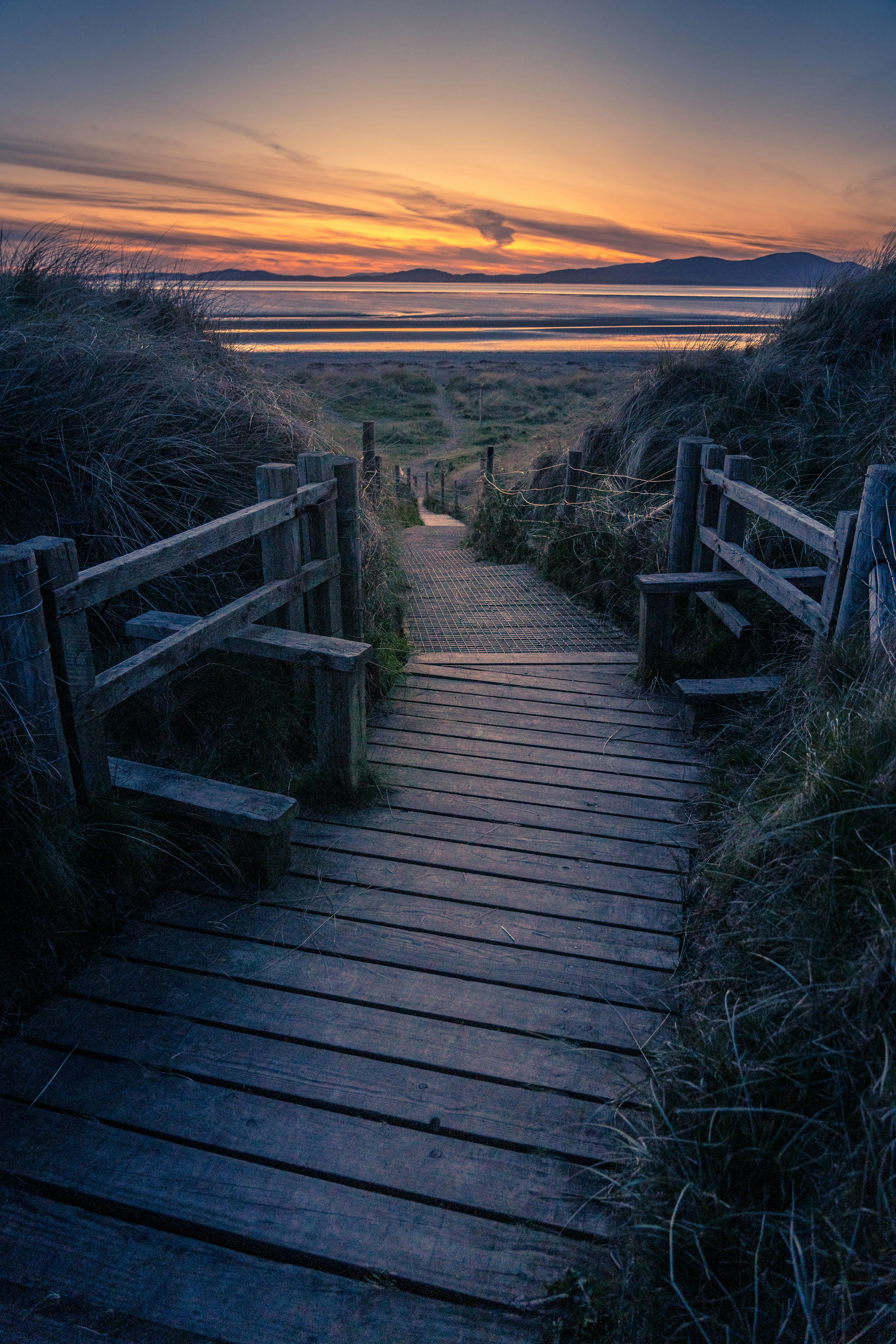 a wooden path leading to the beach at sunset
