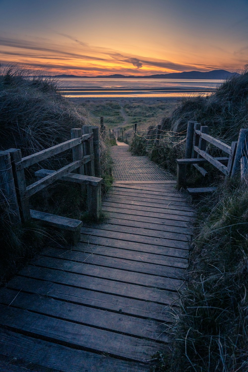 a wooden path leading to the beach at sunset