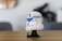 A detailed LEGO model resembling a Star Wars helmet, primarily in white with blue and black accents, is placed on a wooden surface. The background is blurred, indicating a focus on the model.