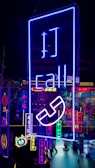 A vibrant display of neon signs with various symbols and text, predominantly featuring a large blue sign with the word 'call' and a telephone icon. The background includes multiple other neon lights in different colors like pink, yellow, and cyan, creating a lively, colorful scene.