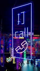 A vibrant display of neon signs with various symbols and text, predominantly featuring a large blue sign with the word 'call' and a telephone icon. The background includes multiple other neon lights in different colors like pink, yellow, and cyan, creating a lively, colorful scene.