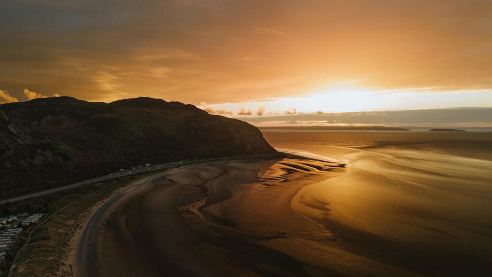 the sun is setting over a beach with a mountain in the background