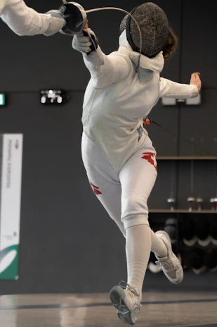 Close-up of a focused athlete in full fencing gear during a competition.