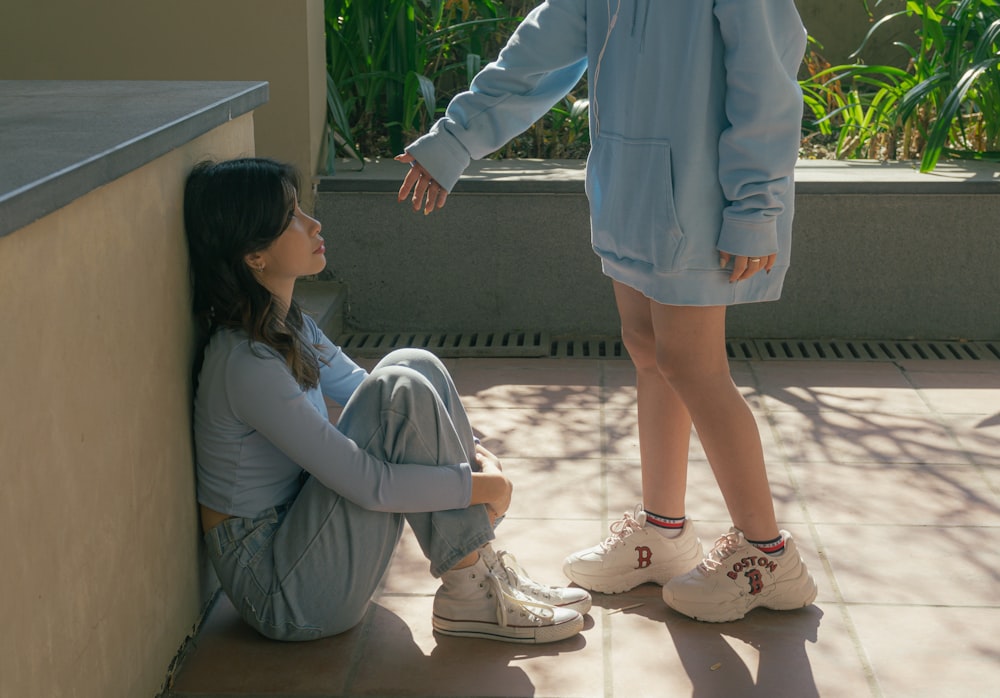 a young girl sitting on the ground next to a woman