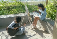 Two people practicing guitar and photography outdoors.