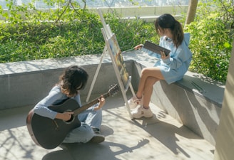 Two people practicing guitar and photography outdoors.