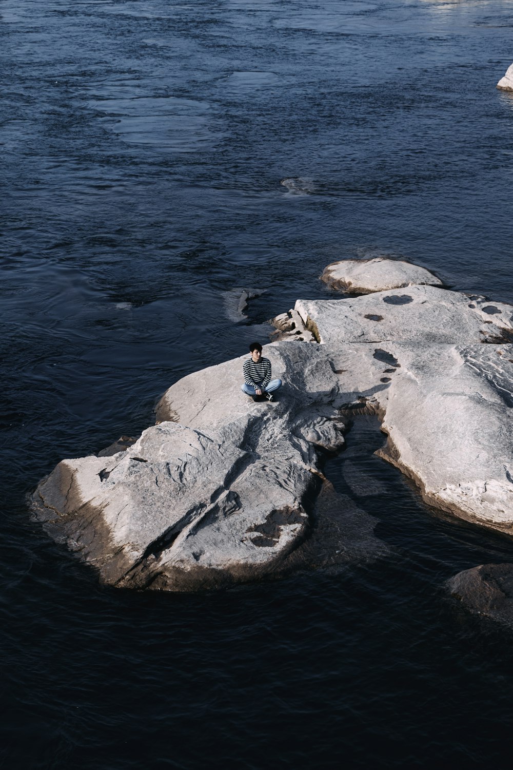 a person sitting on a rock in the middle of a river