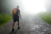 a man with a backpack walking down a foggy road