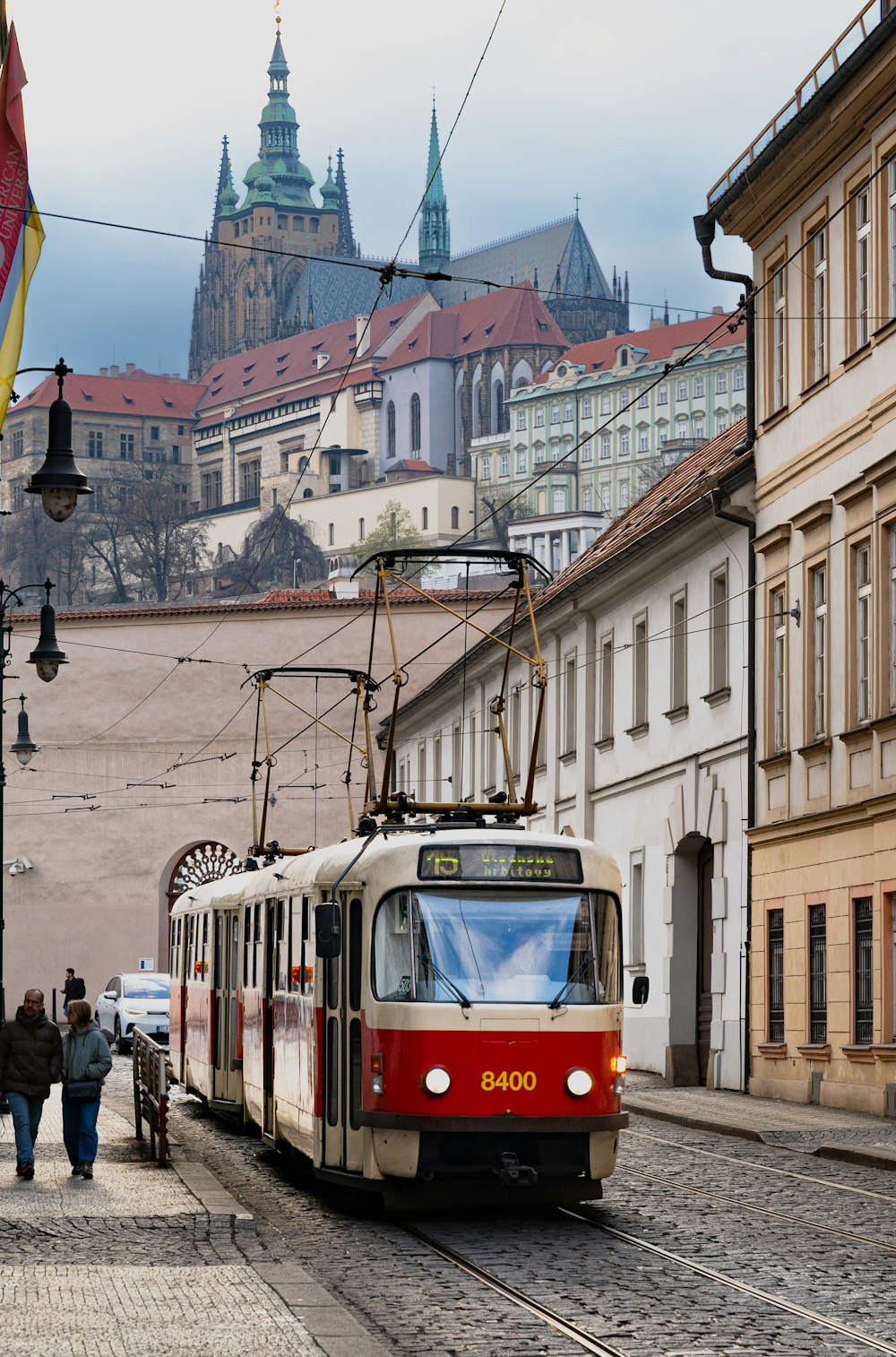 a red and white train traveling down a street next to tall buildings