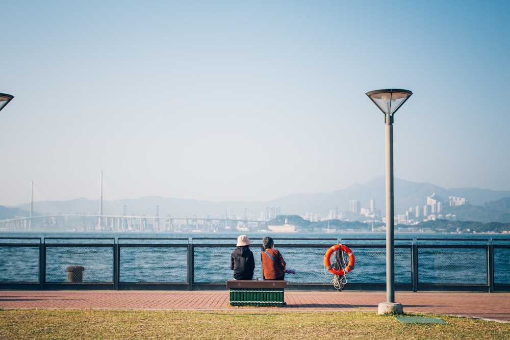 a couple of people sitting on a bench next to a body of water