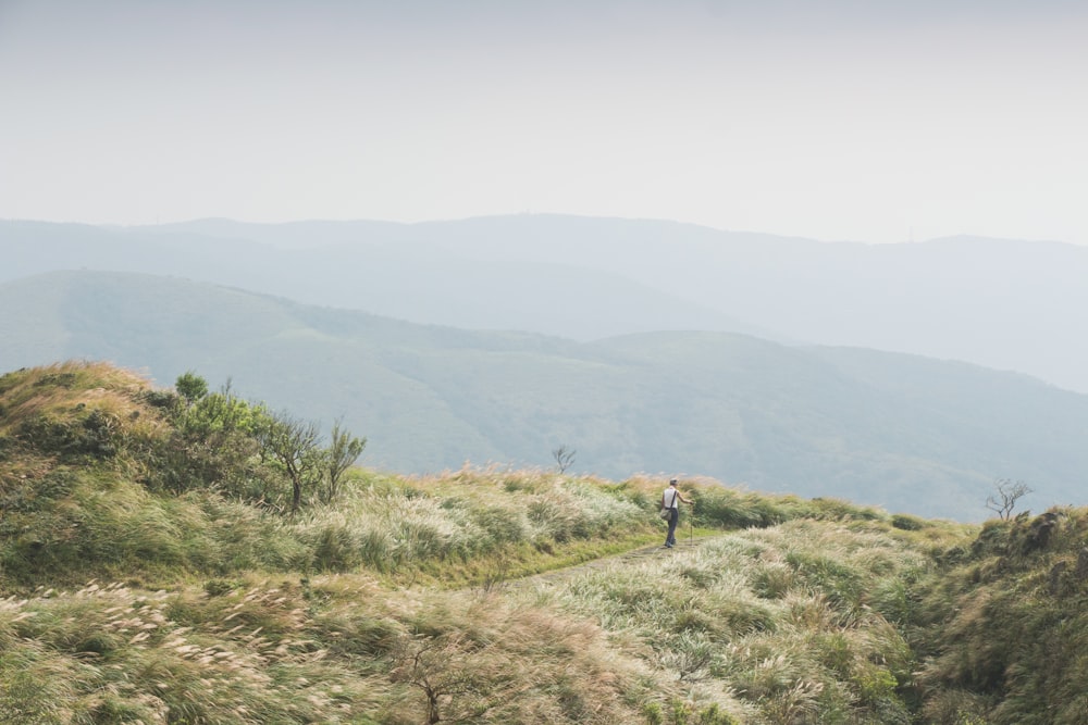 a person hiking up a grassy hill with mountains in the background