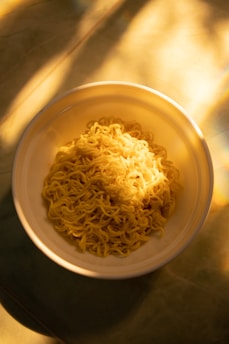A shiny golden Noonug coin character with big sparkling eyes, surrounded by playful noodles and crispy nuggets in a warm, glowing golden world.