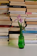 a green vase with a flower in front of a stack of books