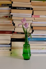 a green vase with a flower in front of a stack of books
