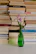 a green vase with a flower in front of a stack of books
