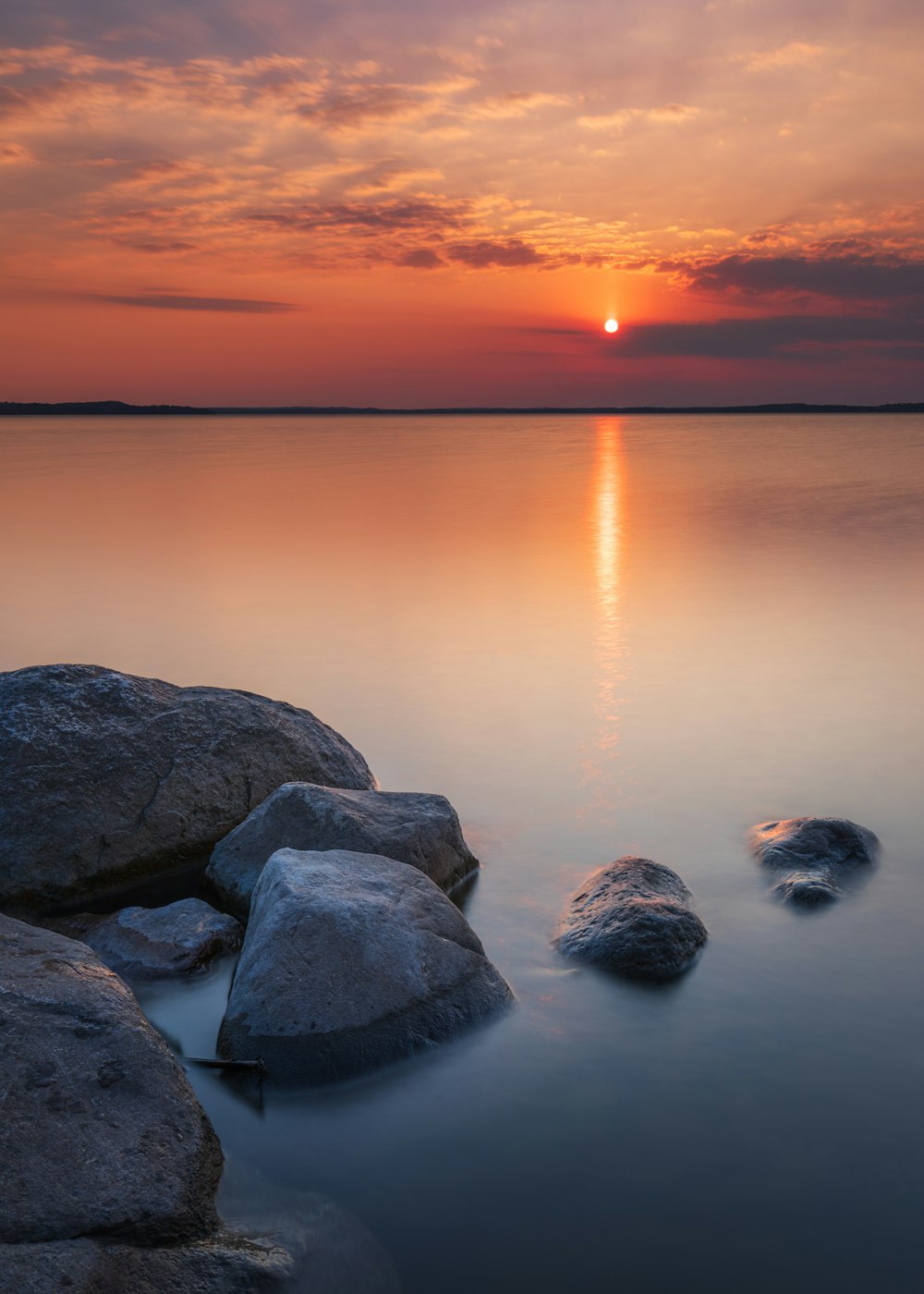 a sunset over a body of water with rocks in the foreground