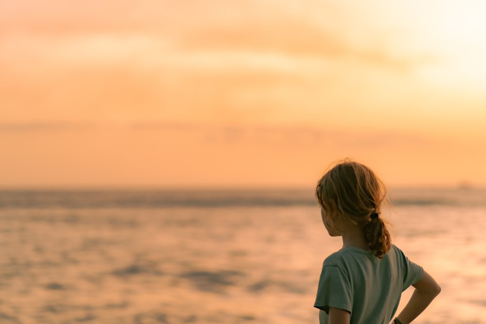 a young girl standing on a beach at sunset