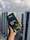 A hand holding a box of Dilmah Ceylon Tea, prominently displayed against a background of high-rise buildings under a cloudy sky. The tea box is dark green with images of tea leaves and a small cup of tea, containing details about the tea blend.