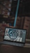 A laptop is displaying an image of a car wheel on its screen, placed on top of cardboard boxes in what appears to be a warehouse. The surroundings are blurred, with visible shelves and boxes in the background.
