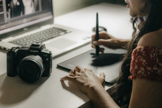 a woman sitting at a desk with a camera and a laptop
