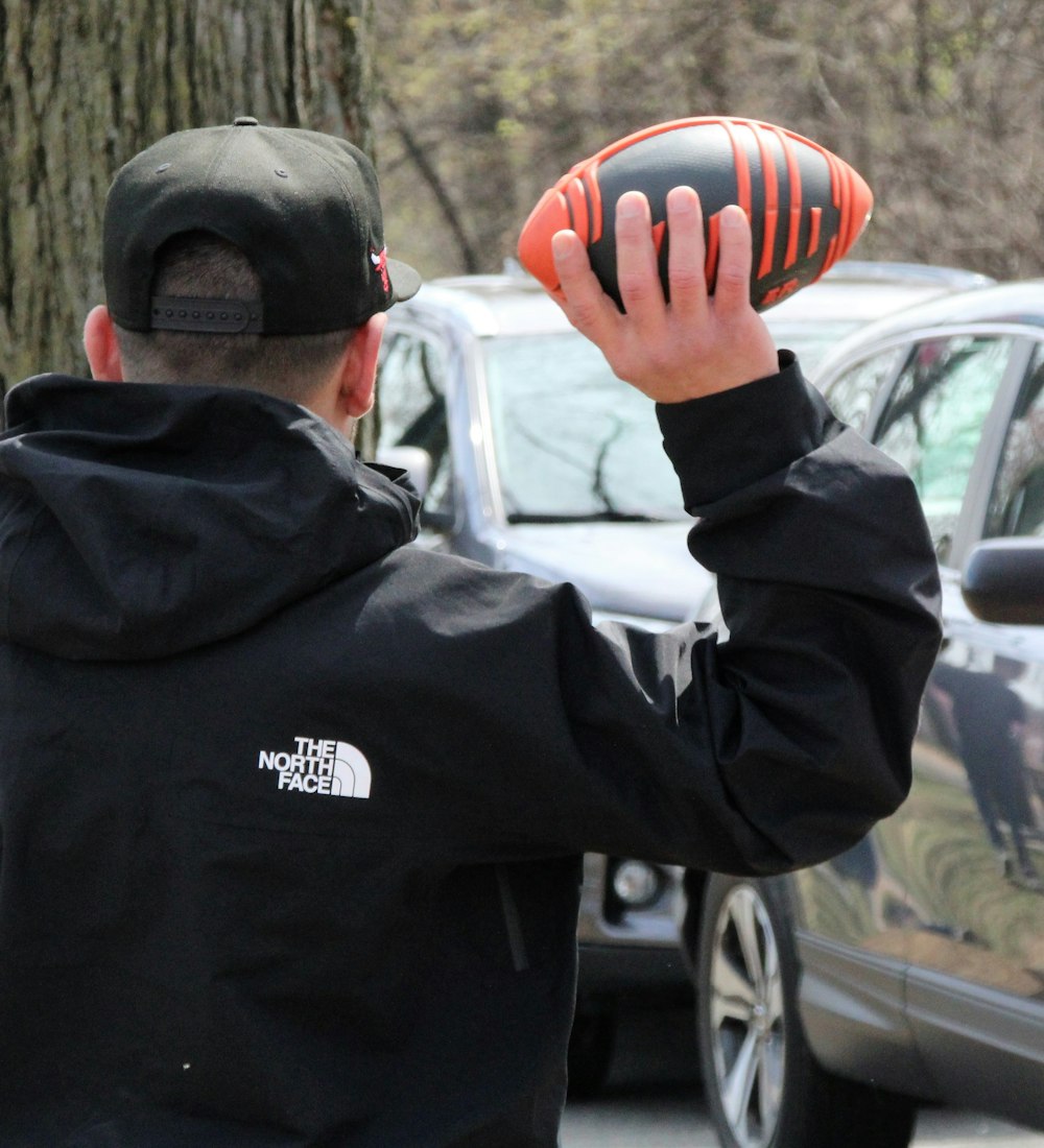 a man in a black jacket holding a black and orange ball