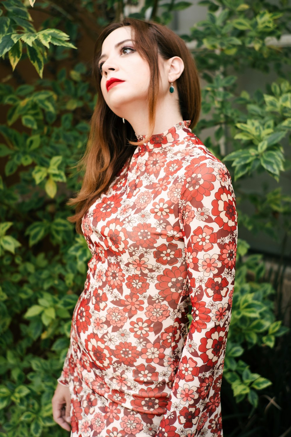 a woman in a red dress standing in front of a bush