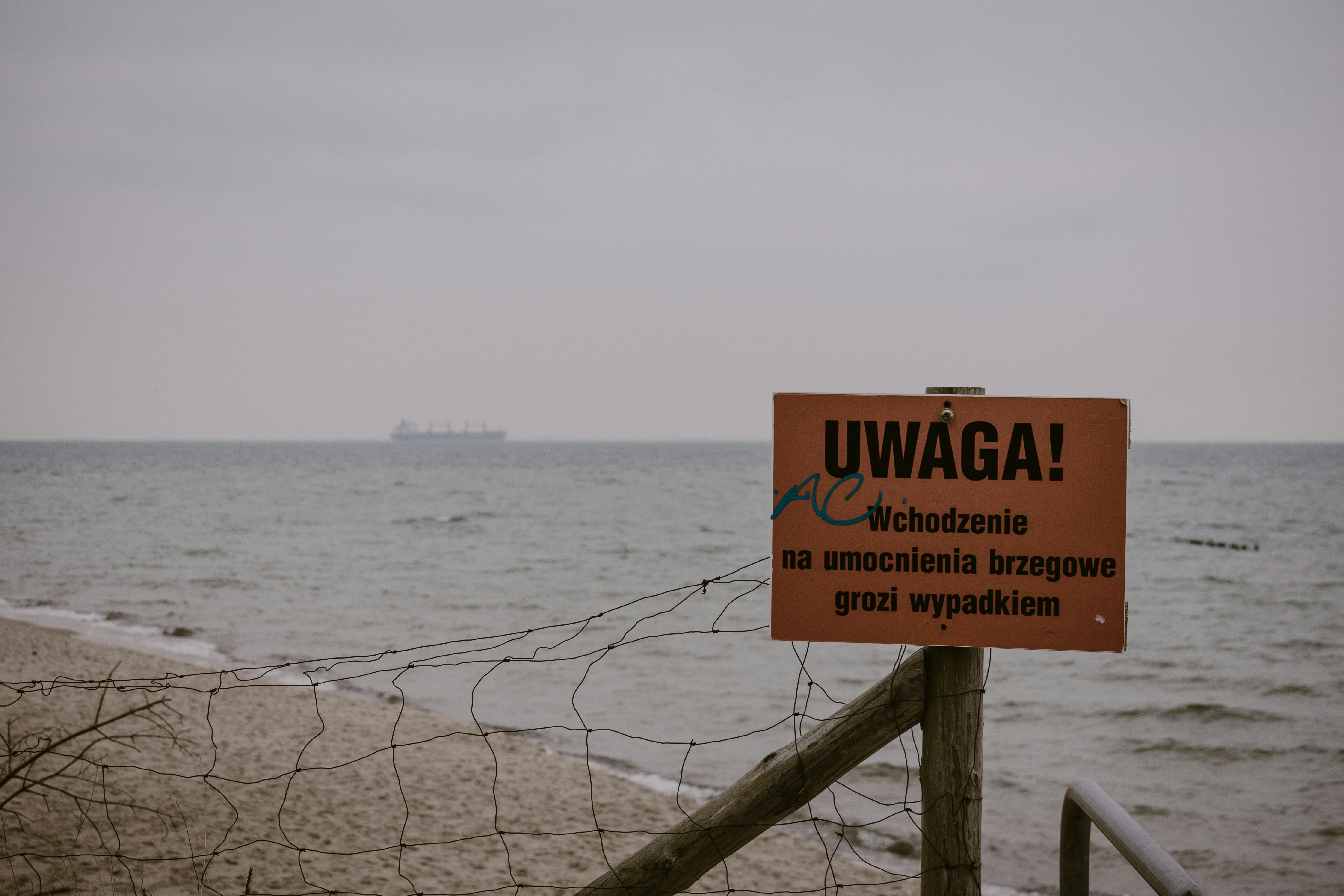 a warning sign on a fence near the ocean