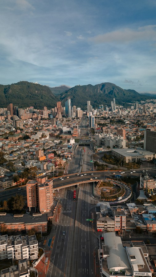 Aerial daytime view of Bogota, Colombia, showing high-rise financial-district skyscrapers, a curving multi-lane highway interchange through dense