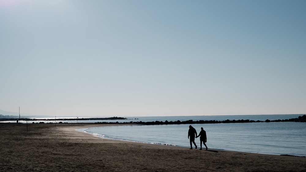 a couple of people standing on top of a sandy beach