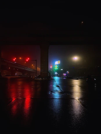 A moody urban nightscape with neon lights casting colorful glows on wet streets.