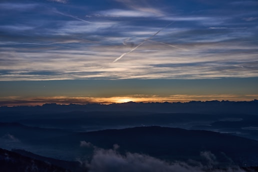 A serene landscape with a sunset over a distant mountain range, symbolizing the end of an era.