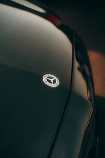 Close-up of a black Dodge Charger emblem on a sleek hood under sunlight.
