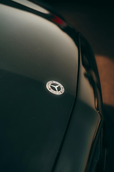A close-up view of a dark-colored car's hood featuring a prominent, metallic emblem in the center. The lighting casts a subtle highlight across the smooth surface, accentuating its sleek design.