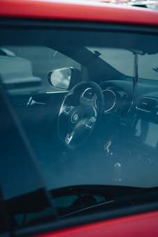 The interior of a car is visible through the window, highlighting a Volkswagen steering wheel, the dashboard, and part of the front seat. The vehicle's interior appears to be modern and well-maintained, and the glass reflects some exterior light.