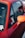 A close-up view of a red car, focusing on the side window and the rear-view mirror. The window displays several stickers, one of which reads 'Get Set Time'. The car's body and side mirror show a strong red and orange palette.