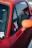 A close-up view of a red car, focusing on the side window and the rear-view mirror. The window displays several stickers, one of which reads 'Get Set Time'. The car's body and side mirror show a strong red and orange palette.