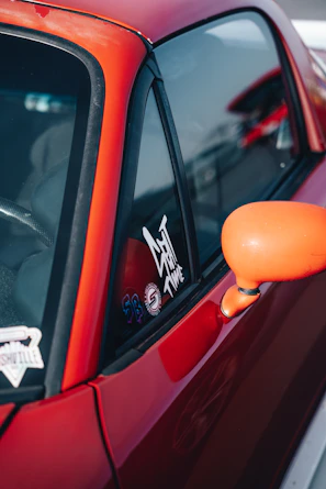 Close-up of a vibrant Mobiluz branded sticker on the rear window of a city car driving through busy streets.