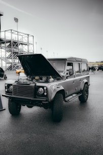 A rugged diesel truck parked on a city street with a technician working on the engine under the open hood.