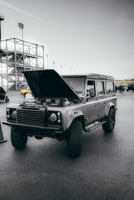 A rugged diesel truck parked on a city street with a technician working on the engine under the open hood.