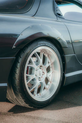 Close-up of a sleek black alloy wheel on a sporty car under soft lighting.