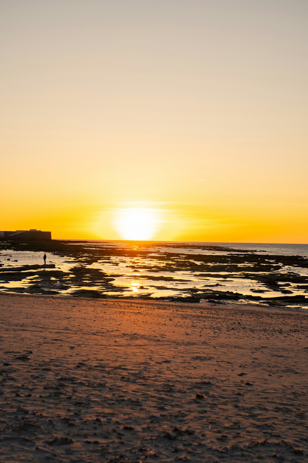 the sun is setting over the ocean with a person walking on the beach